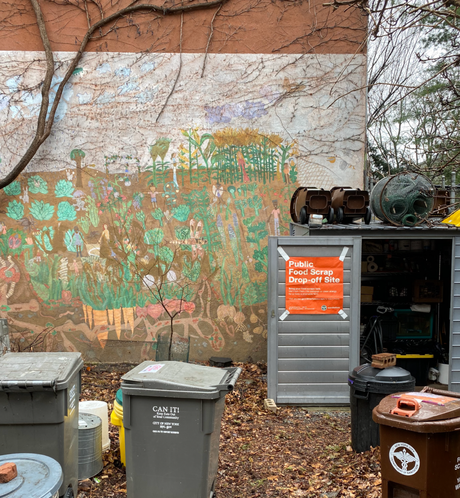 Hand painted mural of garden at El Sol Brillante. There are also multiple recycling bins as well as a gray shed that displays a orange sign reading Public Food Scrap Drop-off Site.
